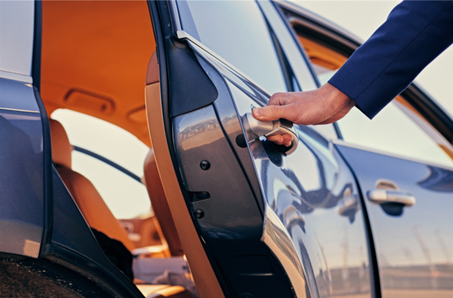 Driver holding a name sign at airport next to a black car